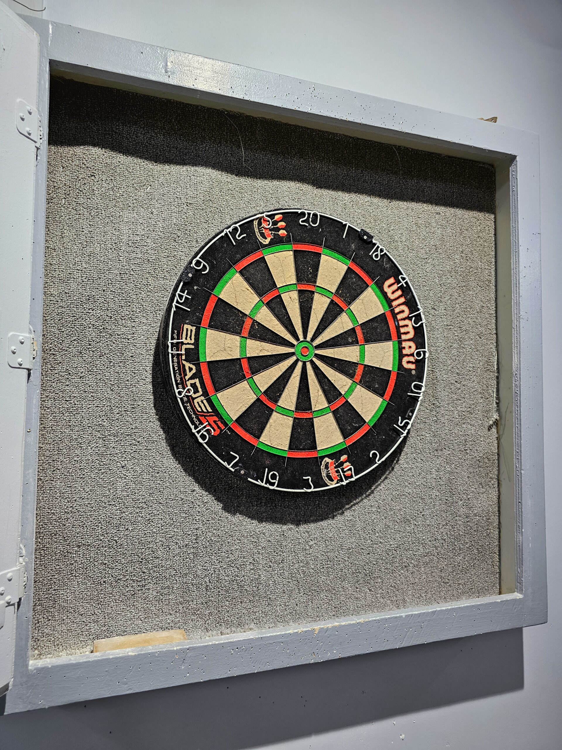 A dartboard is framed by a square of carpeting on a white wall.